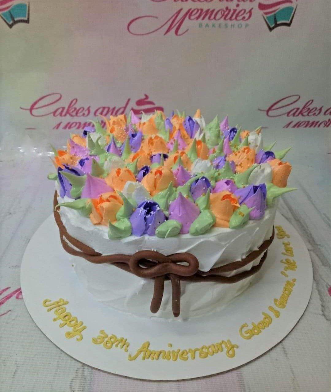 White round cake with a dense top layer of colorful icing tulips in purple, orange, and green, featuring a brown icing bow on the side.