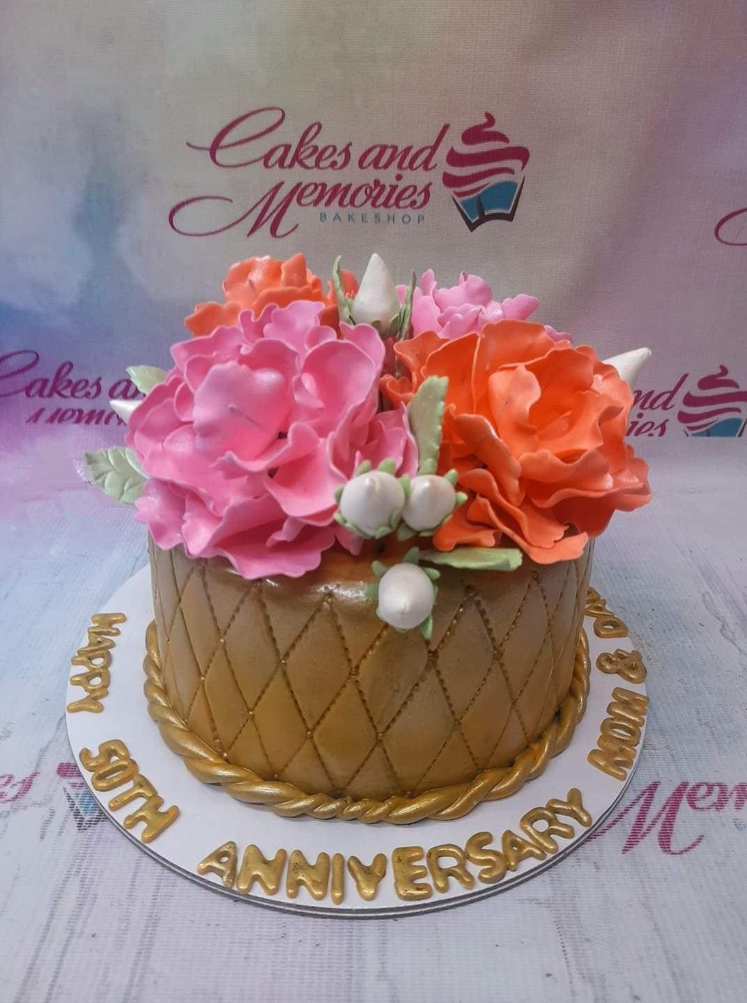 Gold quilted fondant anniversary cake with large pink and orange gumpaste flowers and gold rope border.
