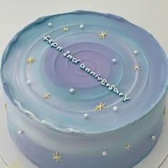A minimalist 1-tier cake with a blue and purple gradient icing, decorated with white pearls and gold stars, featuring a 2nd anniversary message.