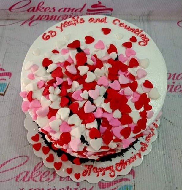 White round cake covered in a dense cluster of red, pink, and white fondant hearts with red icing messages.