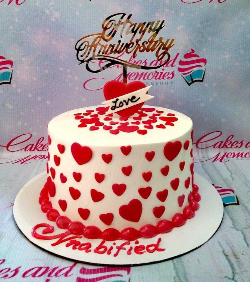 White anniversary cake with red fondant hearts and a gold Happy Anniversary topper.