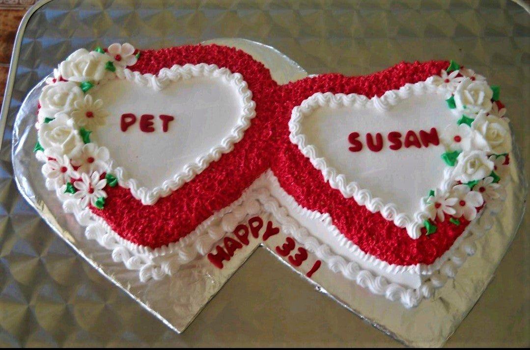 Double heart-shaped red and white cake with white icing roses and red piped messages for a 33rd anniversary.