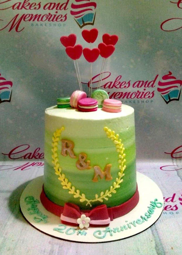 Green gradient anniversary cake with pink macarons, red heart toppers, and a gold wreath design.