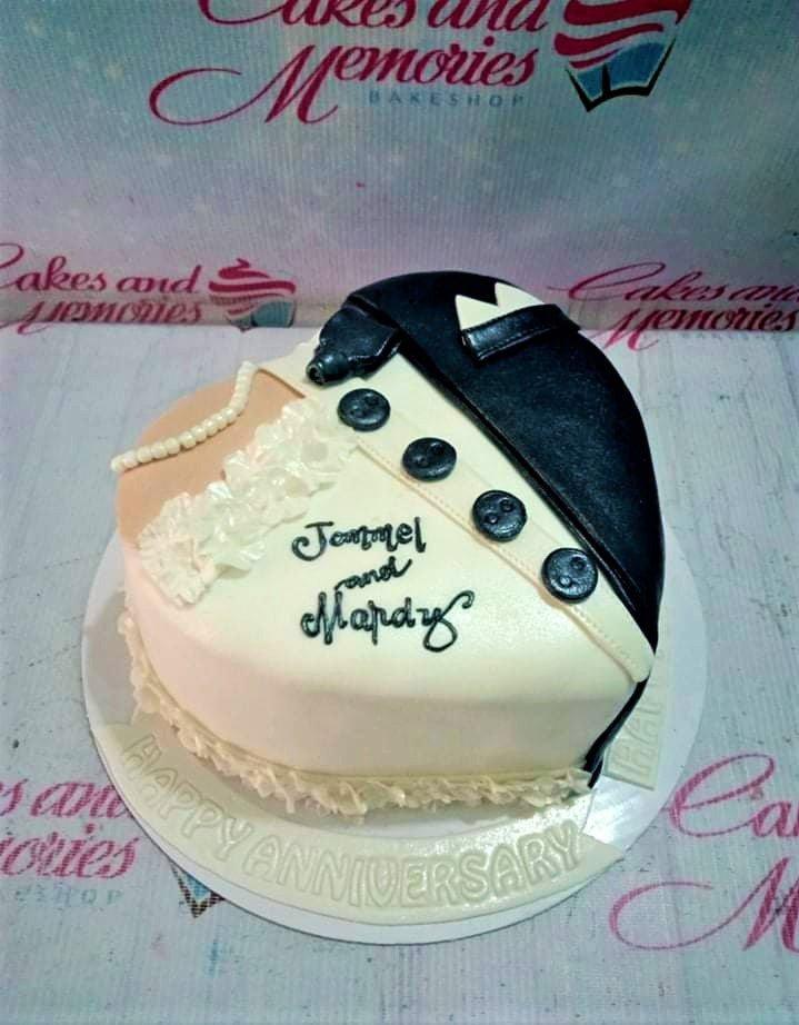 Heart-shaped anniversary cake designed as a tuxedo and wedding dress with black buttons and white ruffles.