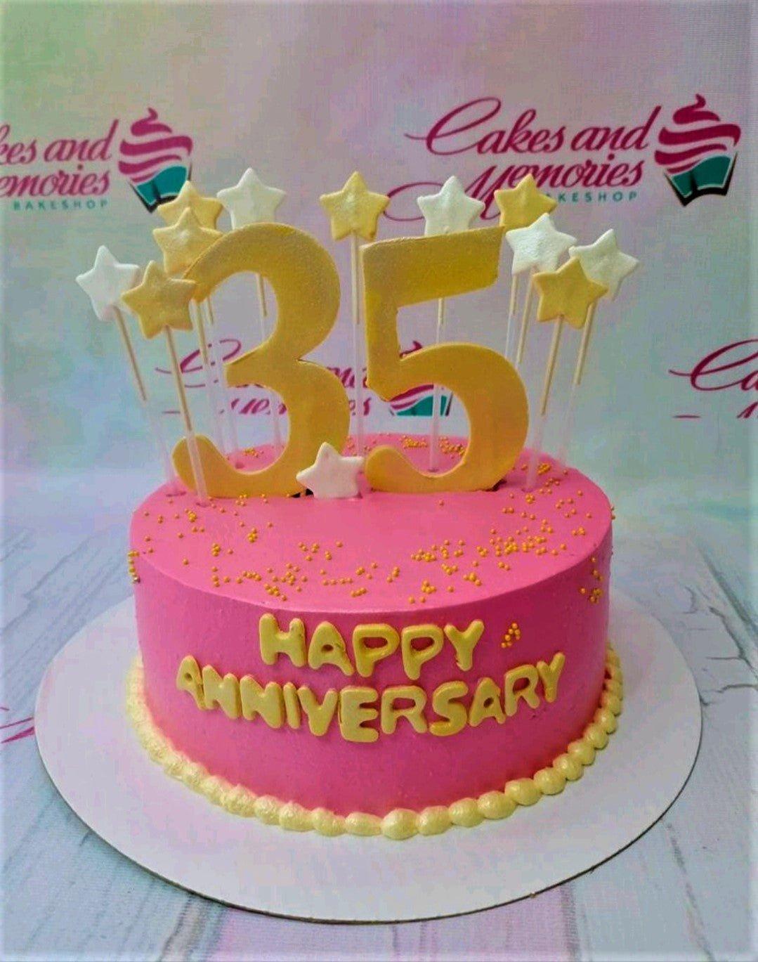 Pink anniversary cake with large gold number 35 topper, gold and white stars, and yellow Happy Anniversary message.
