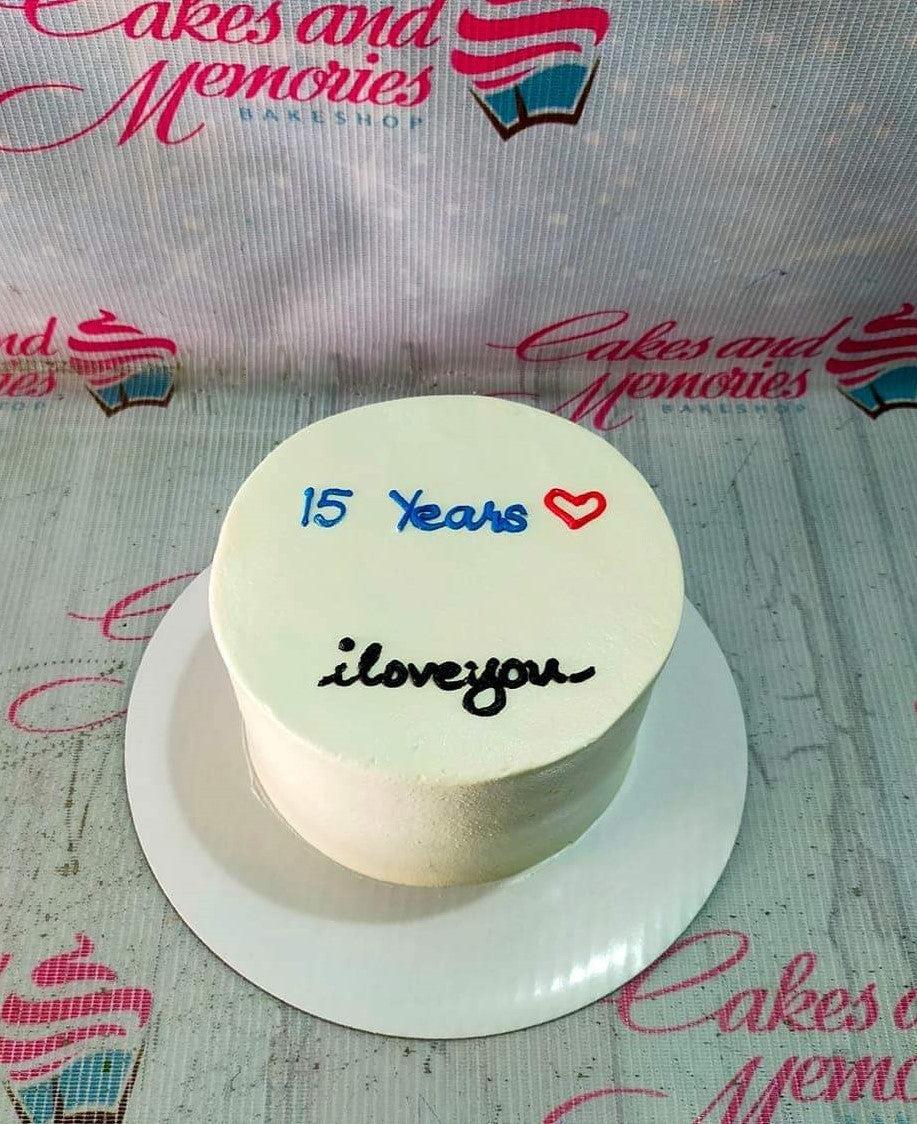 White minimalist bento cake with blue and red icing text and a small red heart for a 15th anniversary celebration.