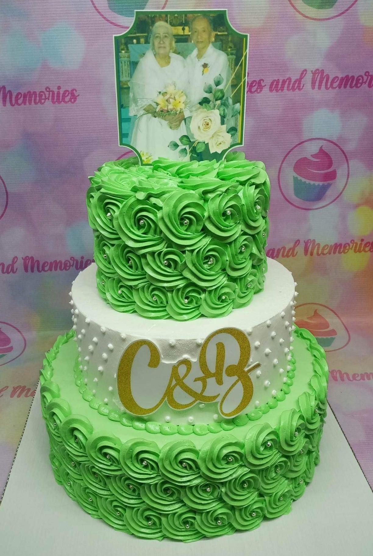 Three-tier green and white anniversary cake with icing rosettes, silver dragees, and a photo printout topper of an elderly couple.