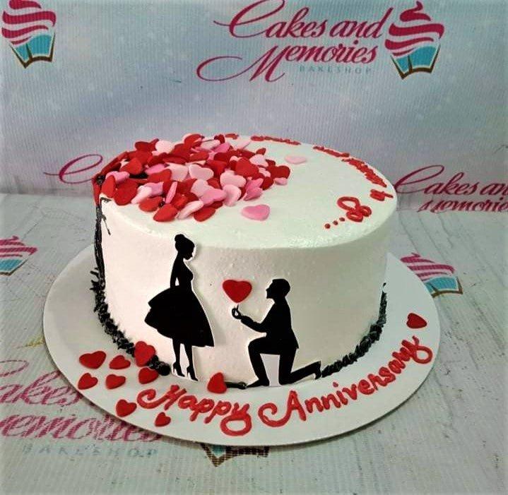 White anniversary cake with black silhouette couple, red hearts, and red icing message on the base board.