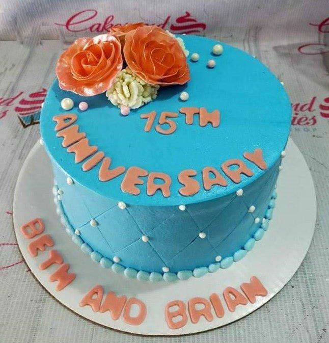 Light blue 15th anniversary cake with orange gumpaste roses, white pearls, and quilted side pattern with pink lettering.