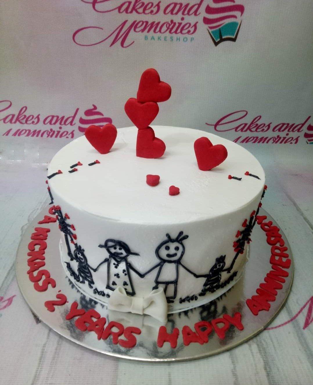 White minimalist anniversary cake with hand-drawn stick figure family and red fondant hearts.