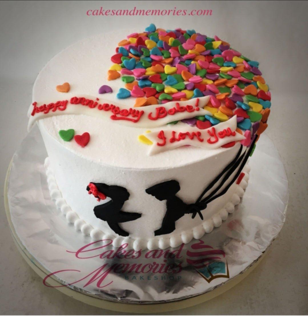 White anniversary cake with a colorful heart balloon design and a silhouette of a couple.