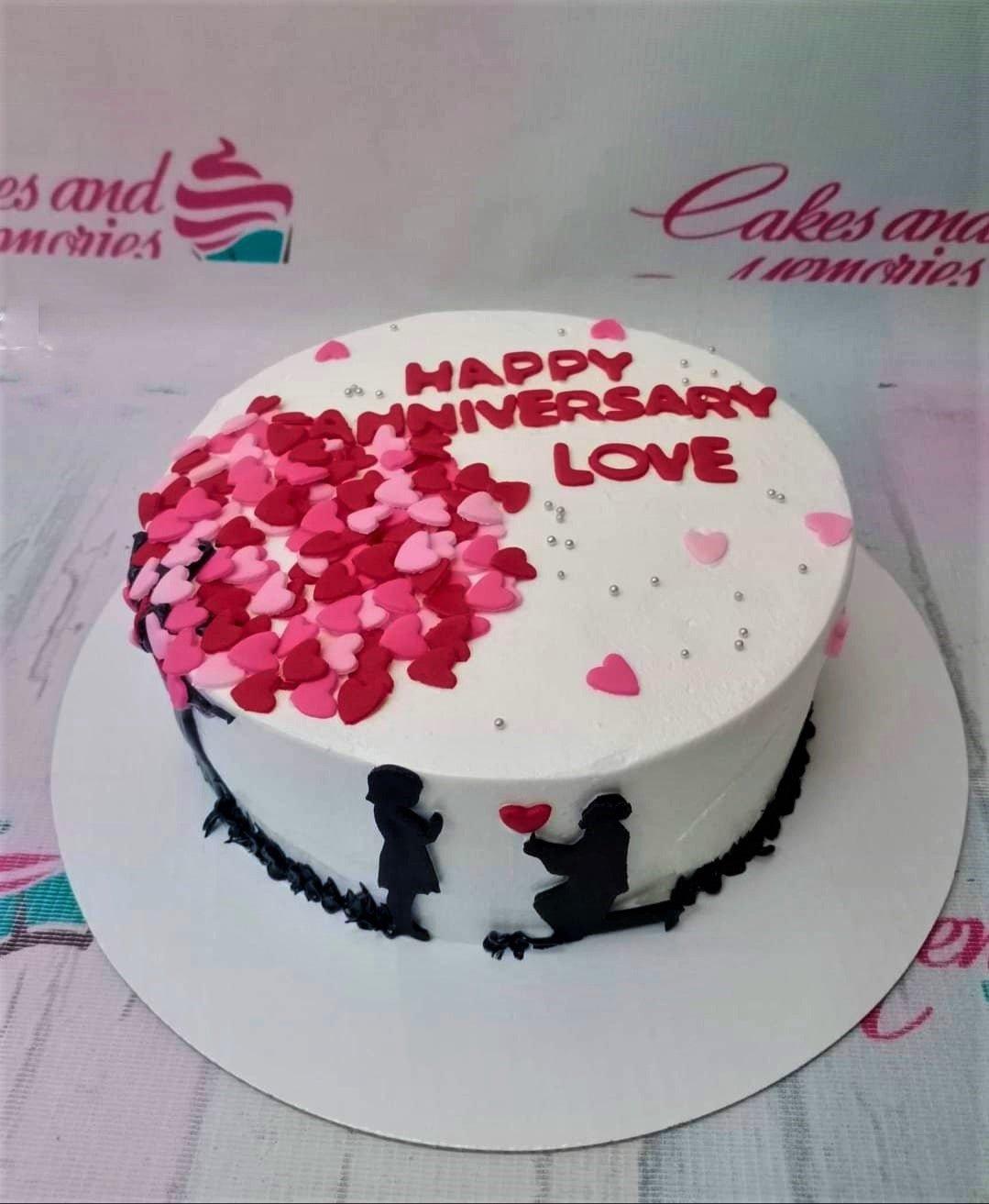 White anniversary cake with a cascade of pink and red fondant hearts and a black silhouette of a couple.