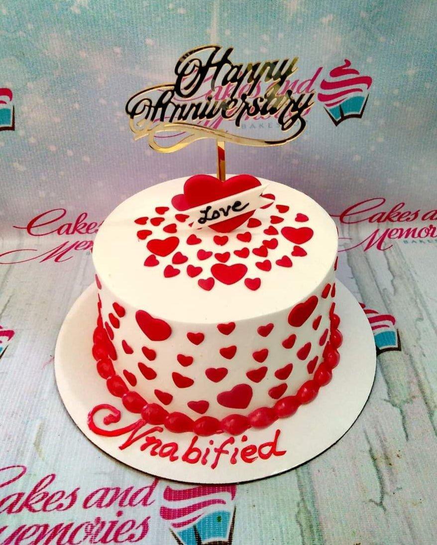 White round anniversary cake decorated with red fondant hearts and a gold Happy Anniversary topper.