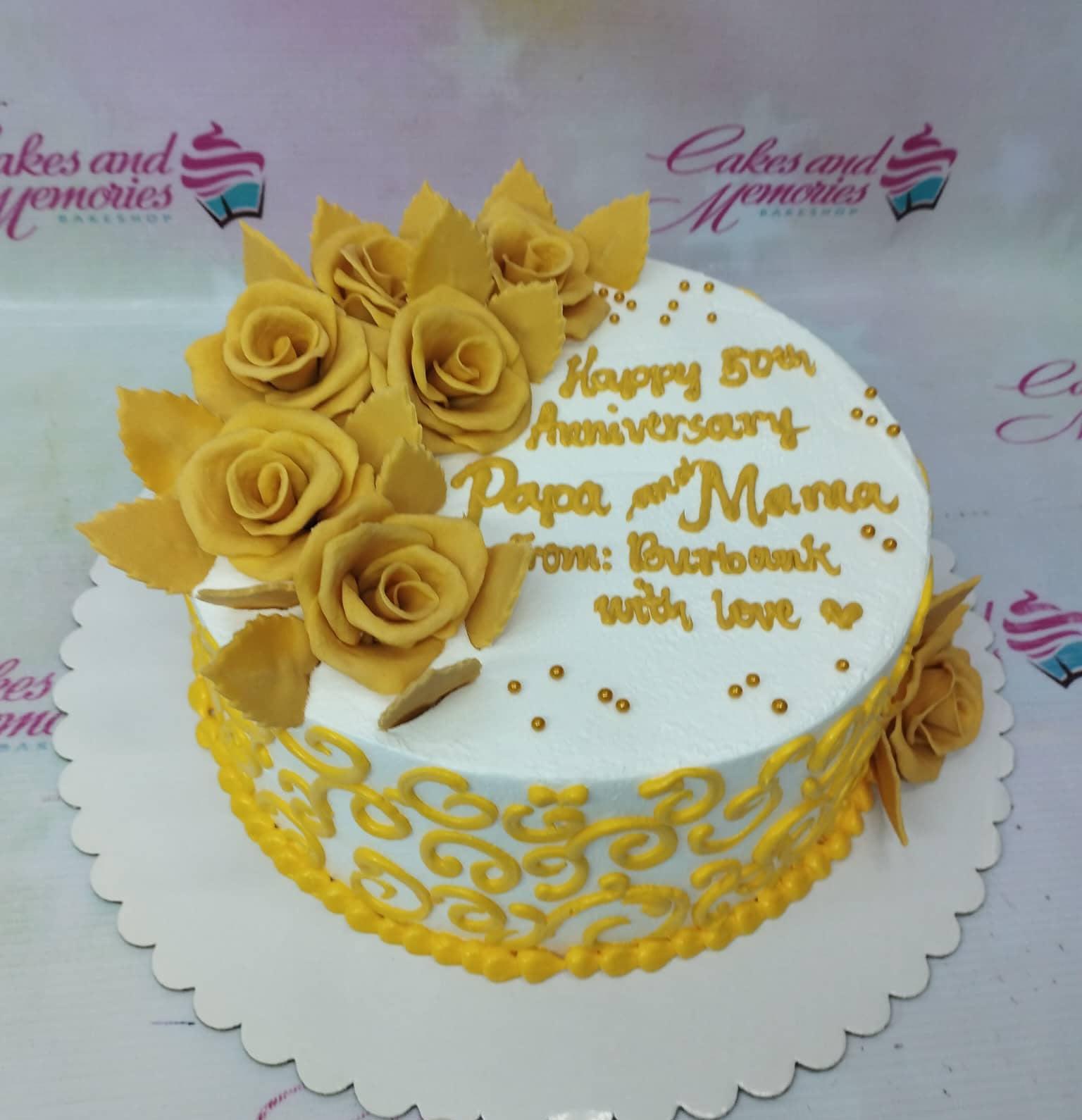 White 1-tier 50th anniversary cake with yellow gumpaste roses, gold dragees, and yellow piped icing swirls on the side.