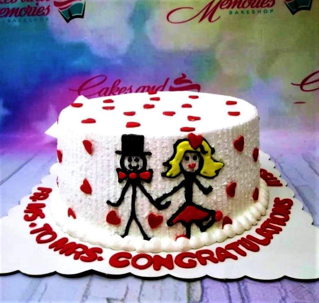 White soft-icing cake with red heart decorations and a hand-drawn stick figure couple holding hands.