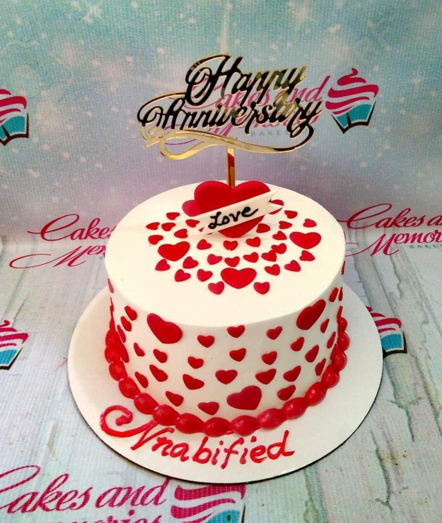 White round anniversary cake decorated with numerous red fondant hearts and a gold Happy Anniversary topper.