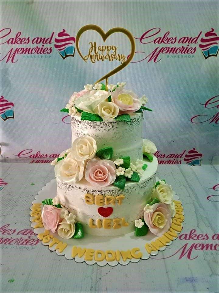 Elegant 2-tier white semi-naked anniversary cake with pink and white sugar roses and a gold heart topper.