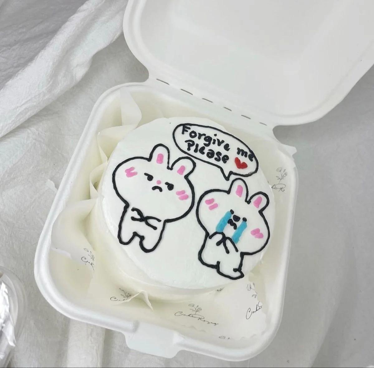 White bento cake with hand-piped sad bunny characters and a speech bubble saying Forgive me Please.