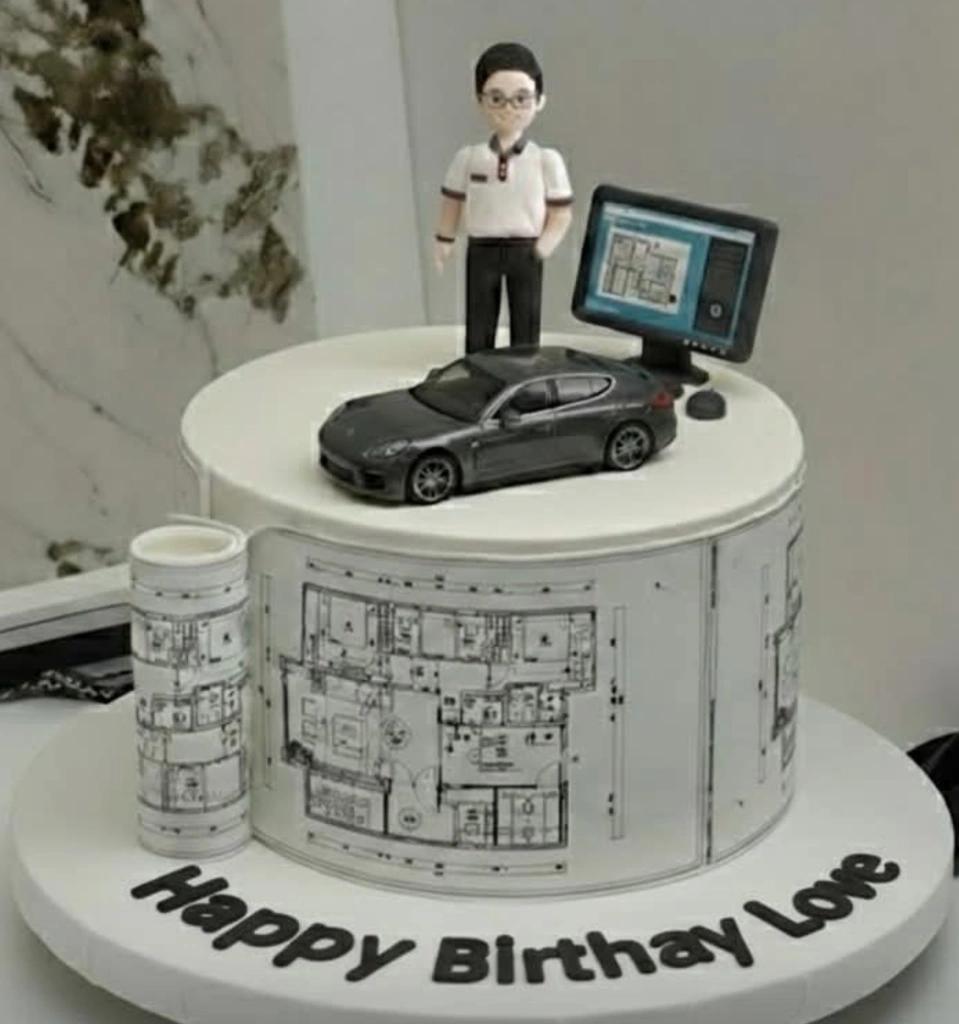White 1-tier architect cake with a fondant man, toy car, computer monitor, and blueprint wrap