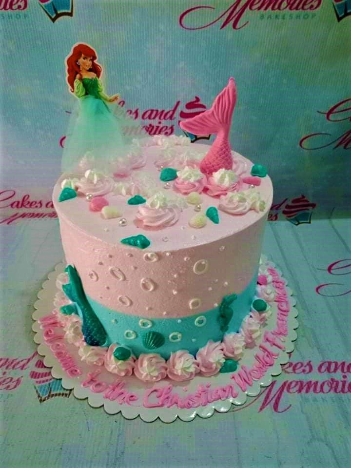 Ariel The Little Mermaid themed cake with pink and teal icing, mermaid tails, and seashell decorations.