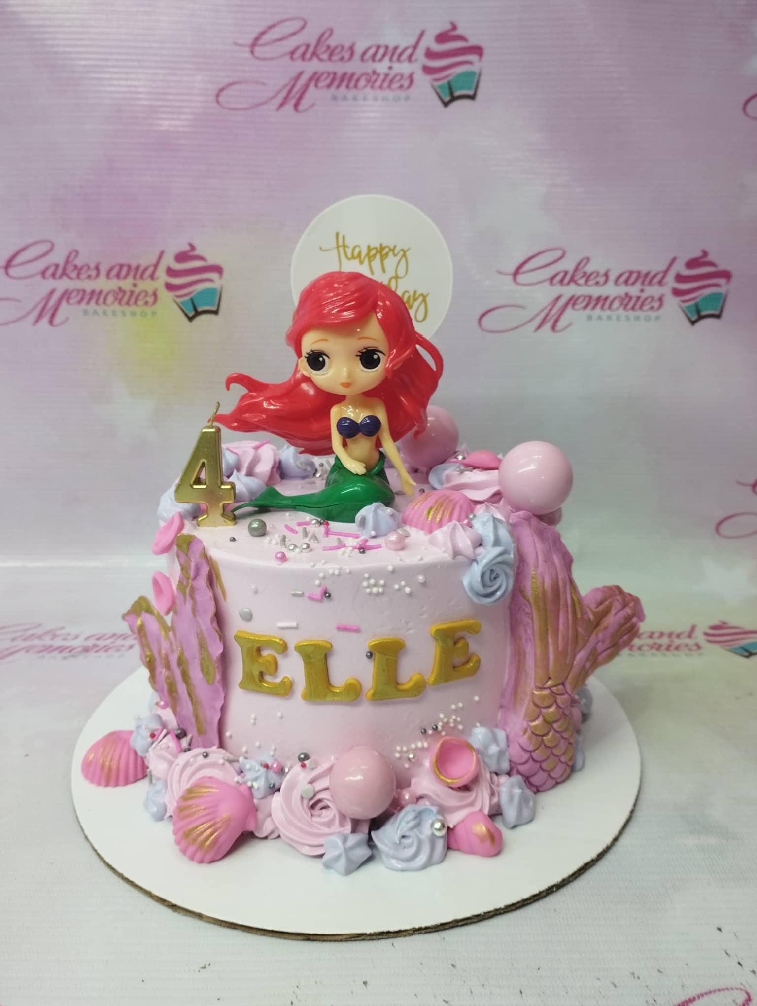 Pink Ariel The Little Mermaid birthday cake with mermaid tail, shells, and gold name topper.
