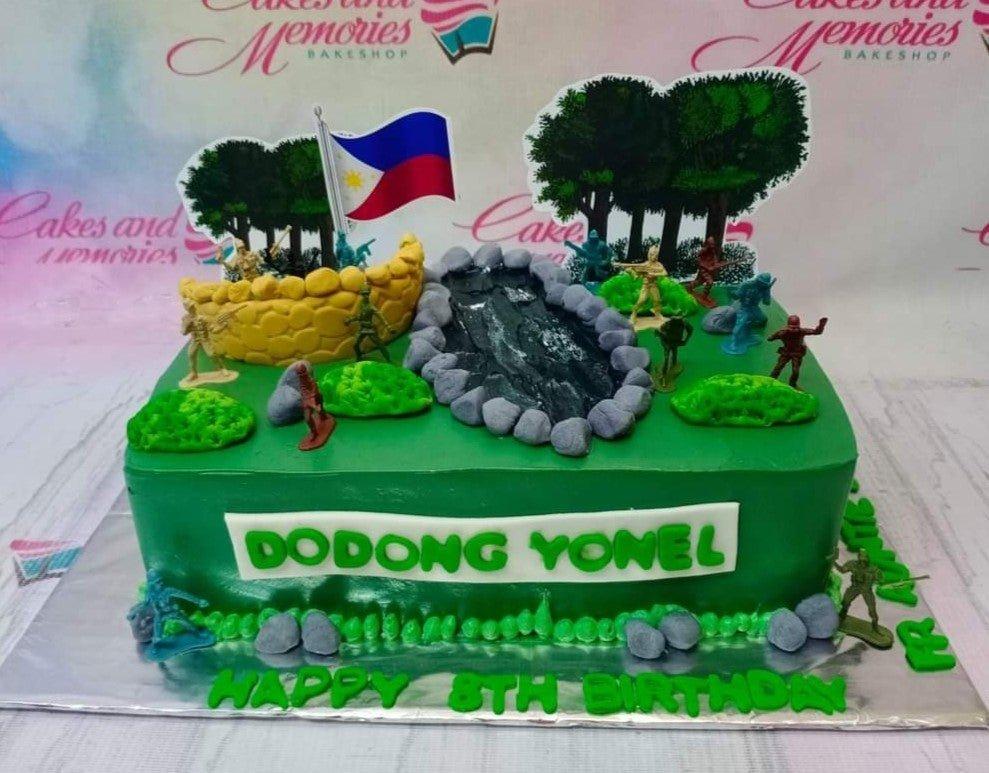 Green rectangle army themed cake with toy soldiers, a Philippine flag, and a fondant river landscape.