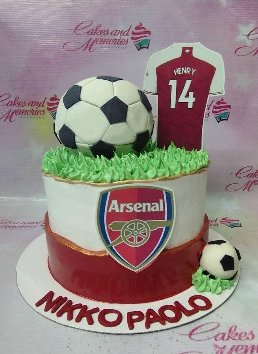 Arsenal football themed cake with a large fondant soccer ball, jersey printout, and Arsenal logo on white and red icing.