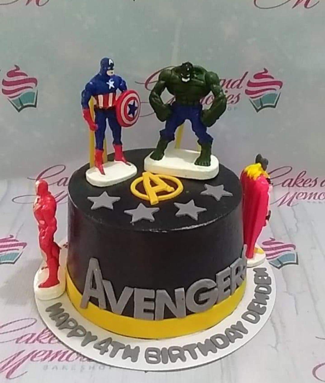 Avengers themed black fondant cake with Captain America, Hulk, Iron Man, and Thor figurines, yellow Avengers logo, and silver stars.