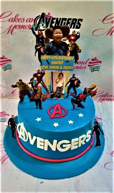 A blue 1 tier cake featuring Avengers character graphics, a child's photo, and a birthday banner, decorated with a red 'A' logo and white stars.