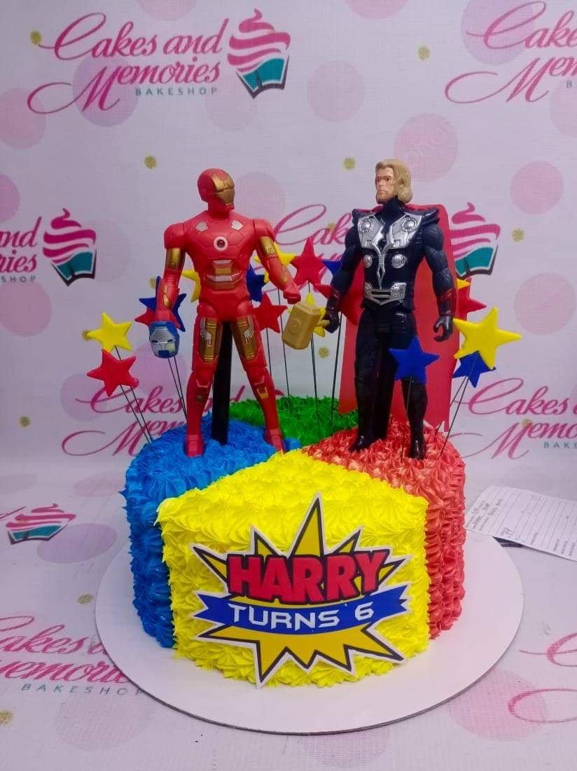 Avengers themed birthday cake with Iron Man and Thor toy figures on red, yellow, and blue textured icing.