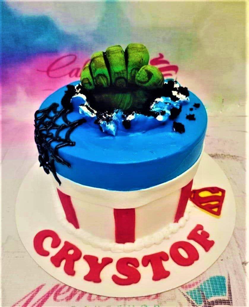Avengers themed birthday cake featuring a green Hulk fist smashing through blue icing with Superman and Spider-Man accents.