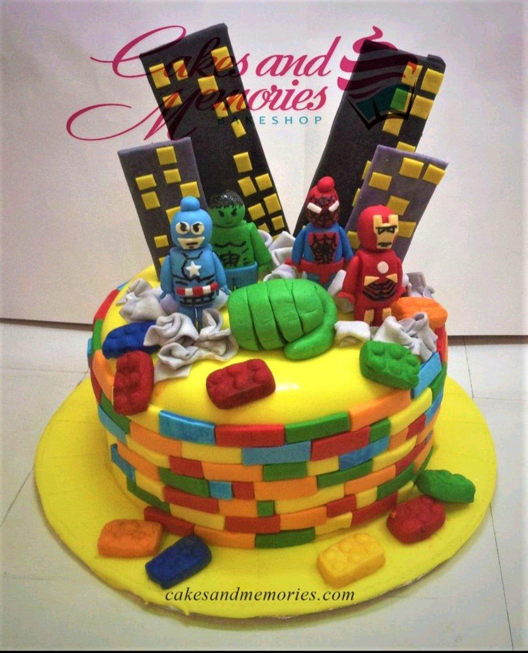 Avengers Lego themed birthday cake with Hulk, Iron Man, Captain America, and Spiderman figurines on a yellow fondant base with colorful Lego bricks.
