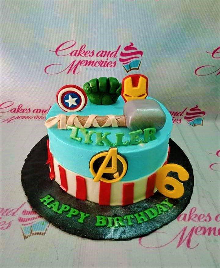 Avengers themed birthday cake with Thor's hammer, Hulk's fist, Captain America's shield, and Iron Man's mask toppers.