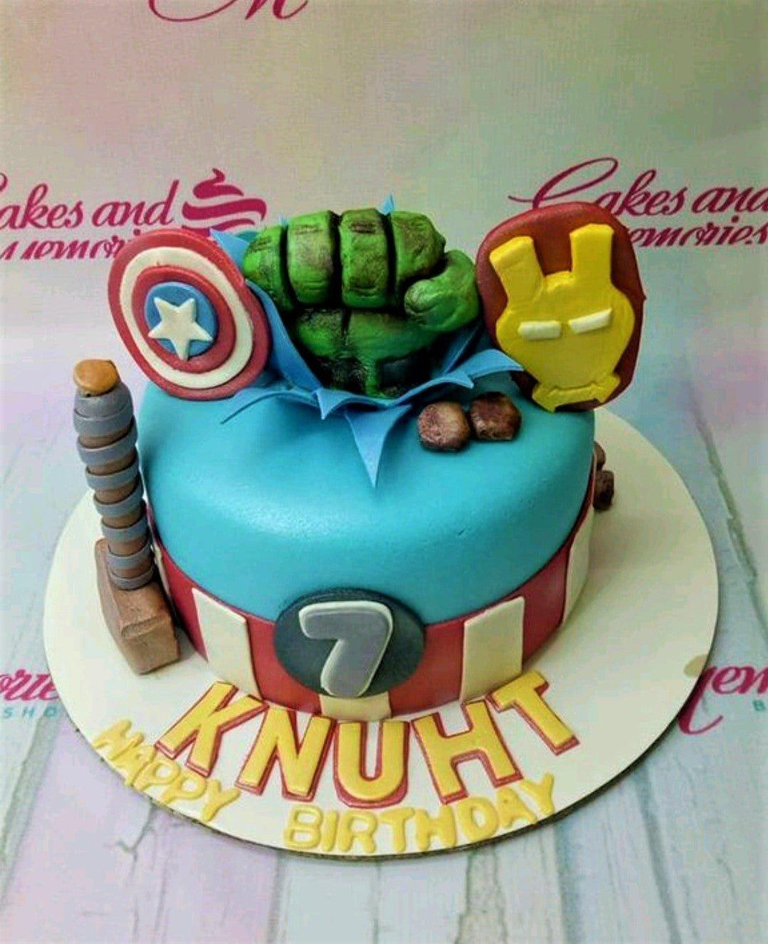 Avengers themed blue fondant cake with Hulk fist, Captain America shield, Iron Man mask, and Thor's hammer toppers.