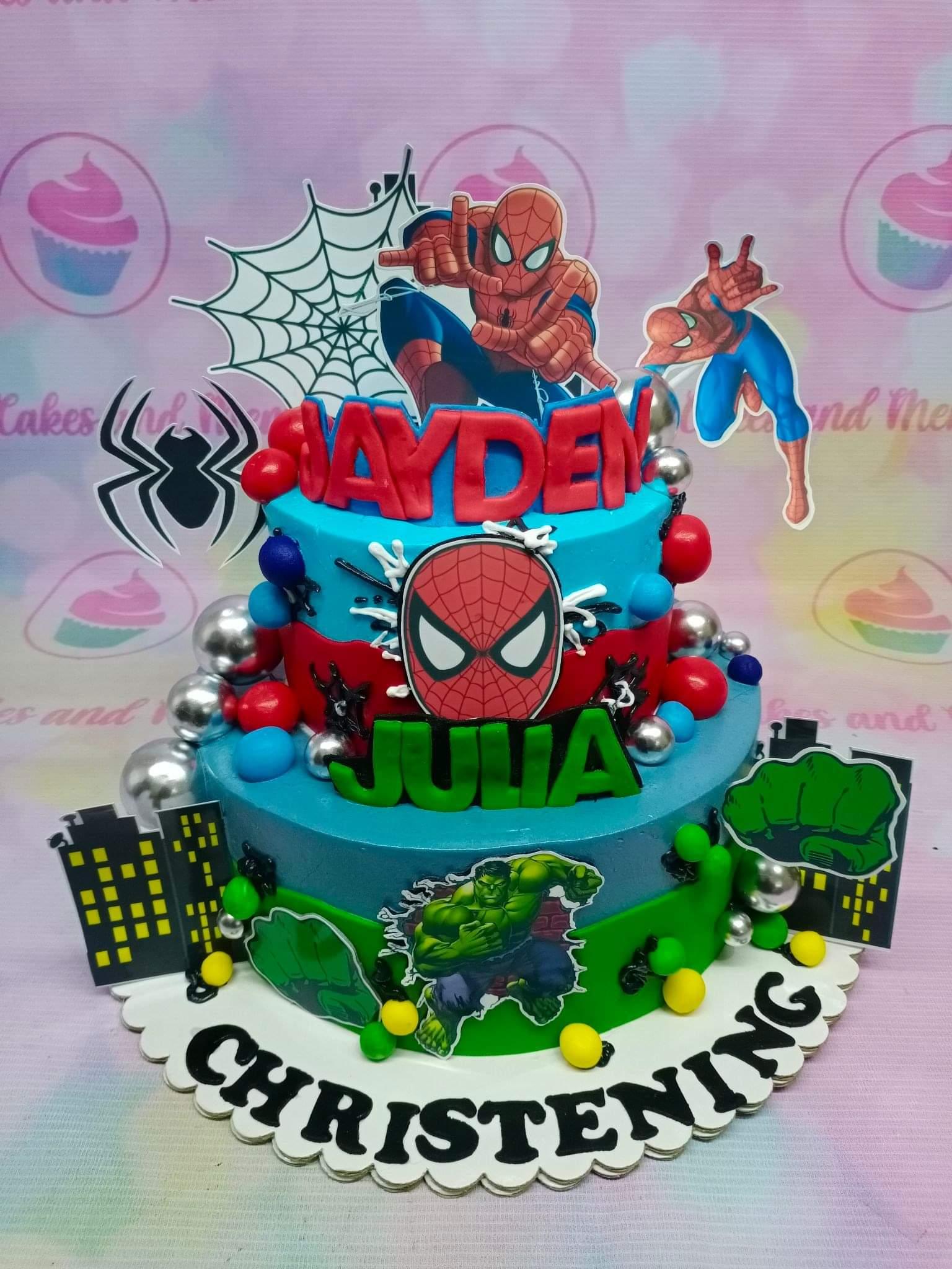 Two-tier Avengers themed cake featuring Spiderman, Hulk, and city skyline decorations in blue, red, and green.