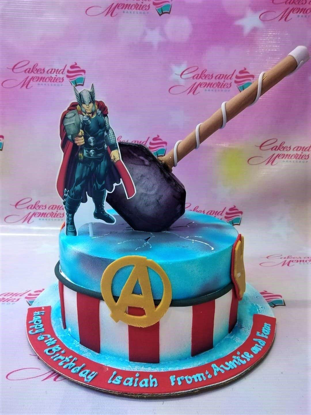 Avengers themed cake featuring Thor and Mjolnir hammer on a blue and red striped fondant base.