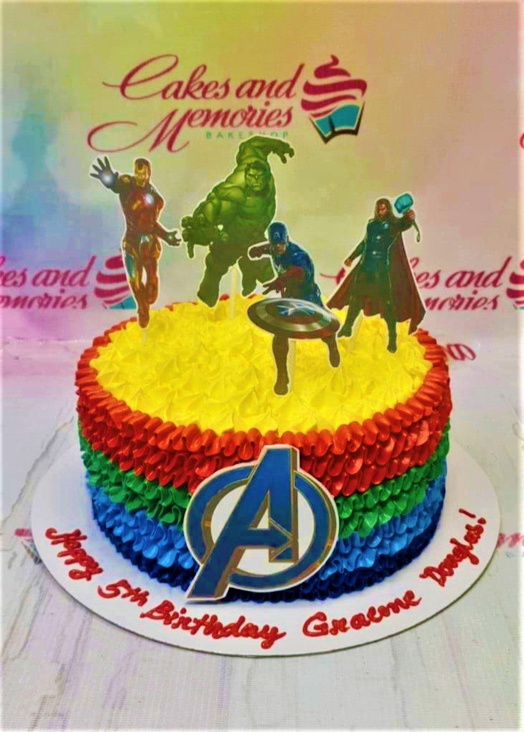Avengers themed birthday cake with colorful ruffled icing layers in red, green, blue, and yellow, topped with superhero character cutouts.