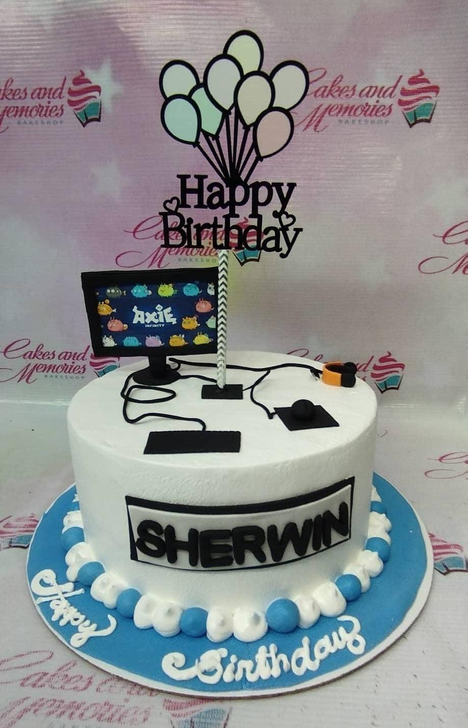 White gaming themed cake with Axie Infinity monitor printout, fondant keyboard, mouse, and headset toppers with a balloon birthday topper.