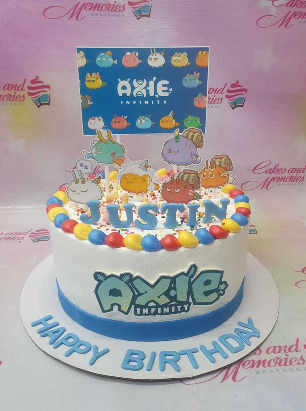 Axie Infinity themed birthday cake with colorful icing borders and character printouts for Justin.