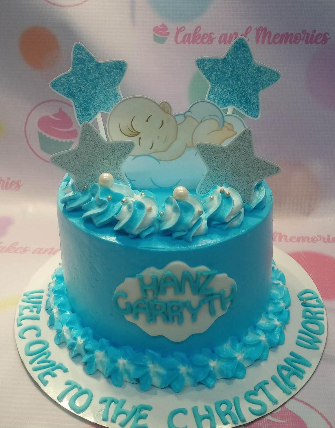 Light blue 1-tier baby boy baptism cake with sleeping baby printout, glitter stars, and blue and white icing rosettes.