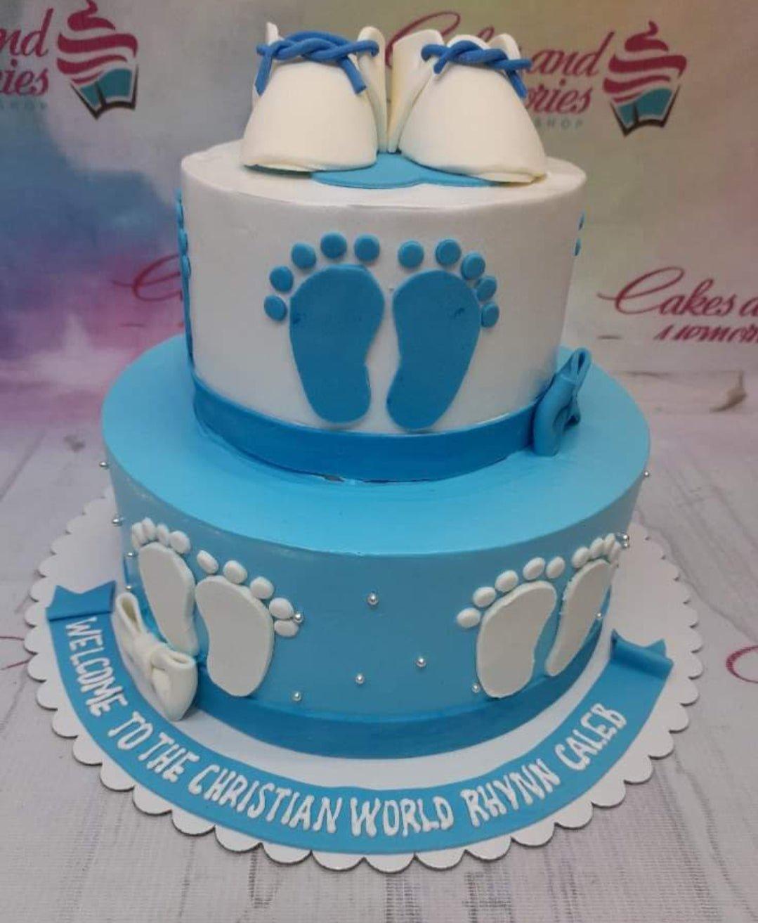 Two-tier blue and white baby shower cake with fondant baby shoes and footprints.