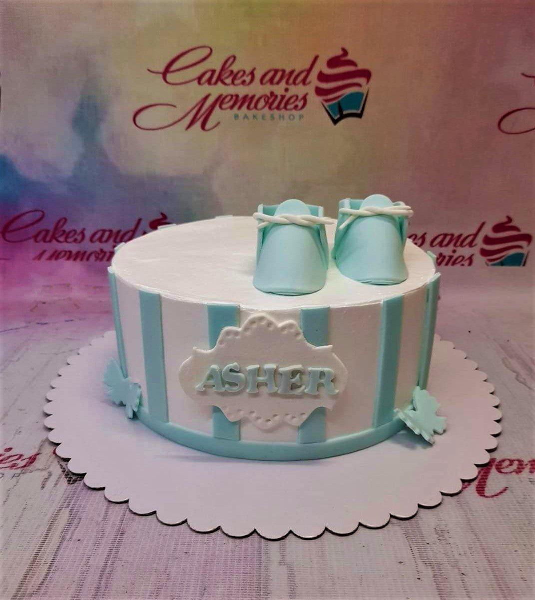 White and light blue striped baby shower cake with fondant baby shoes and name plaque