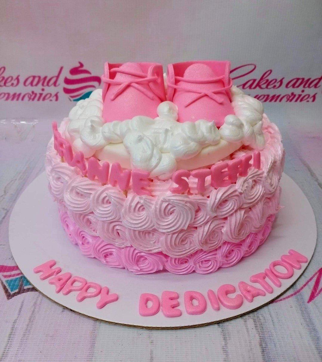 Pink ombre rosette cake with pink fondant baby shoes and white icing clouds on top.