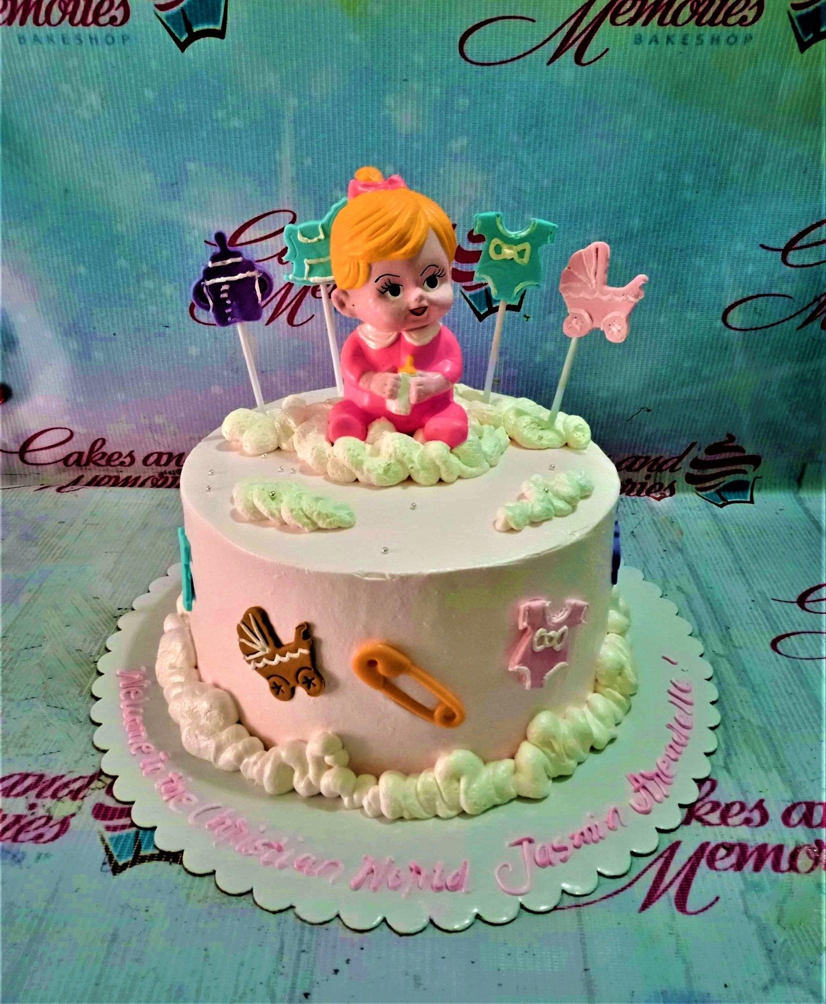 Pink baby girl baptism cake with a 3D baby figure, clouds, and baby-themed fondant decorations like a stroller and safety pin.