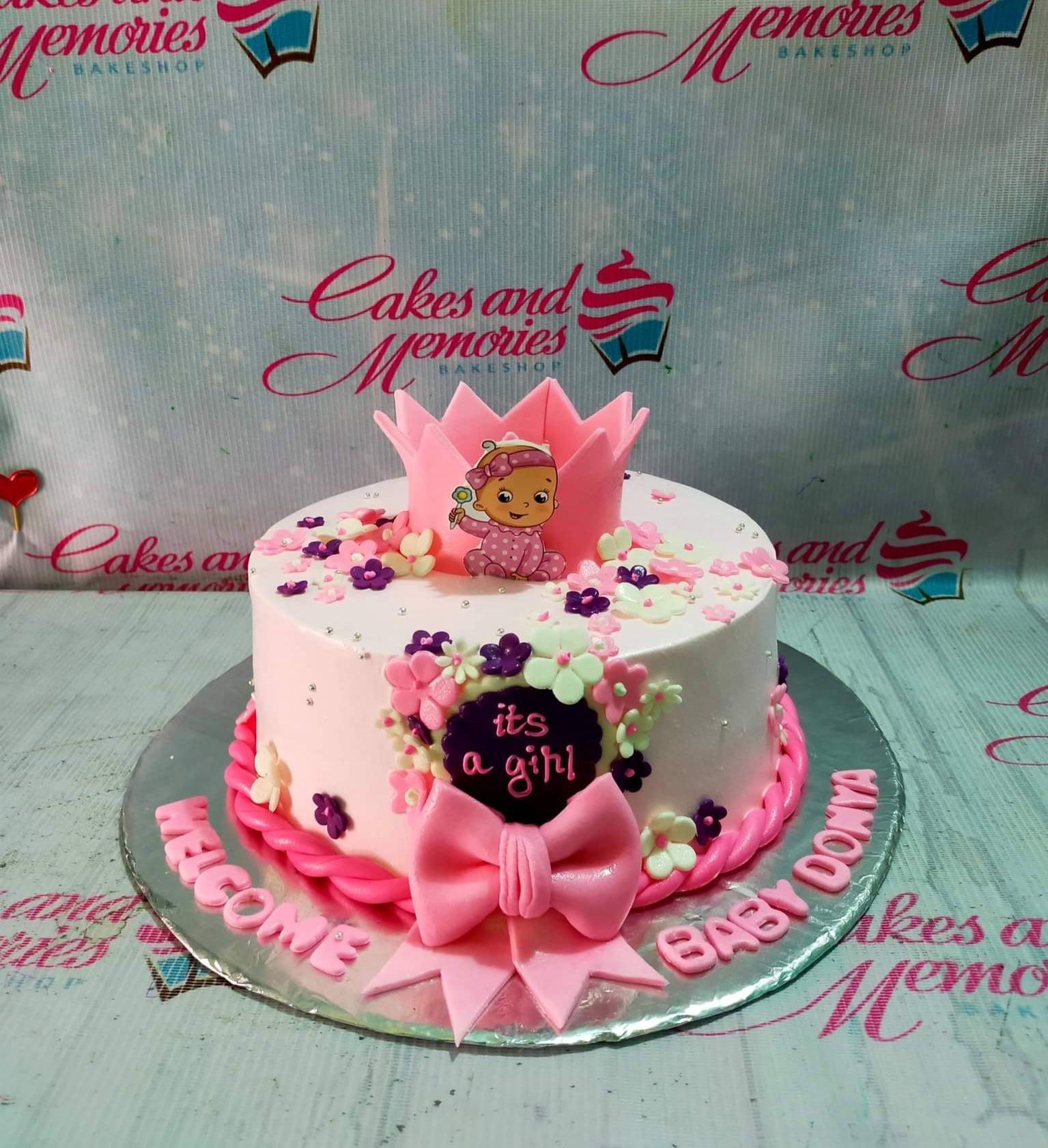 Pink baby girl cake with a pink crown, baby printout, fondant flowers, and a large pink bow.