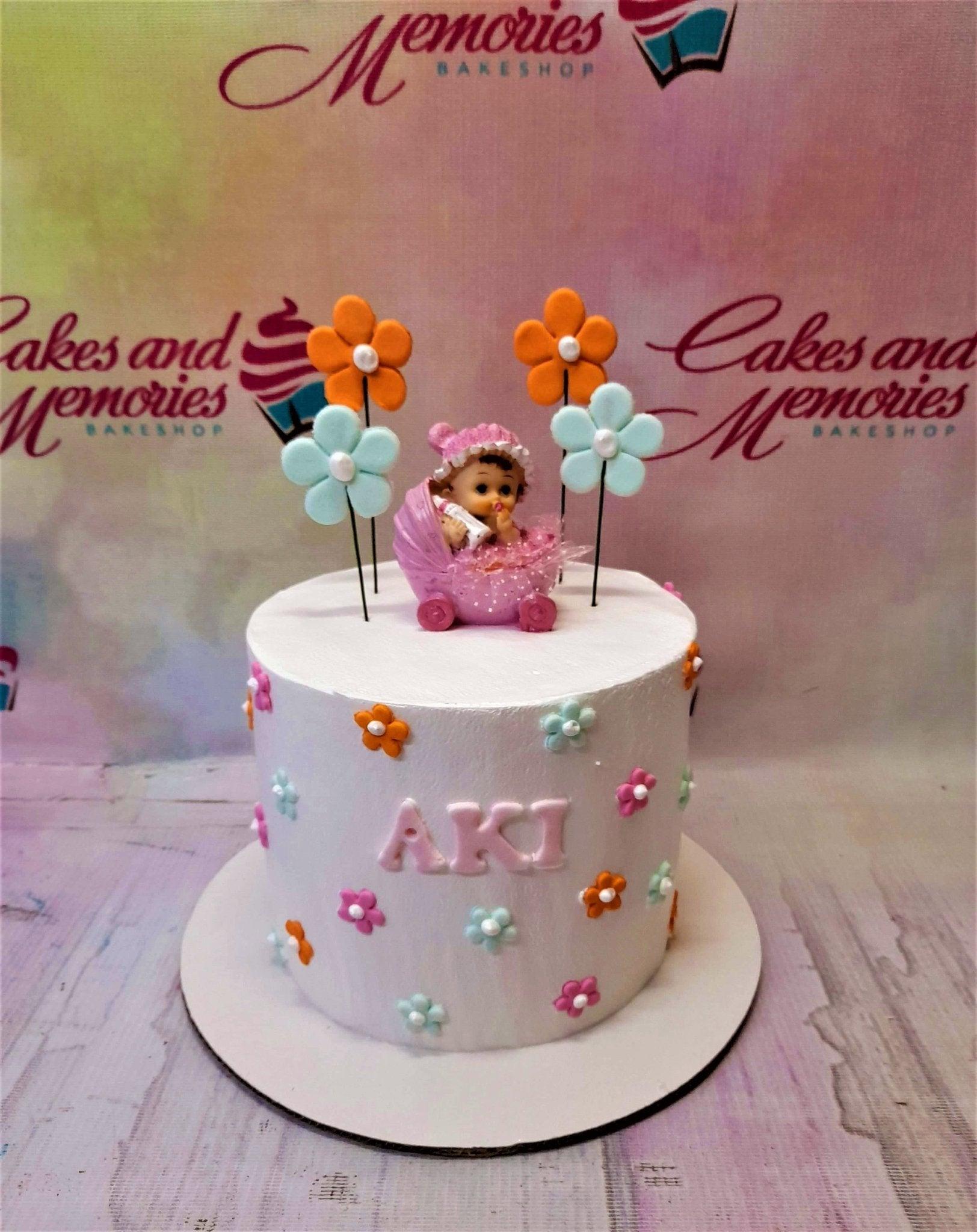 White 1-tier baby girl birthday cake with a pink baby figurine in a stroller and colorful fondant flowers.