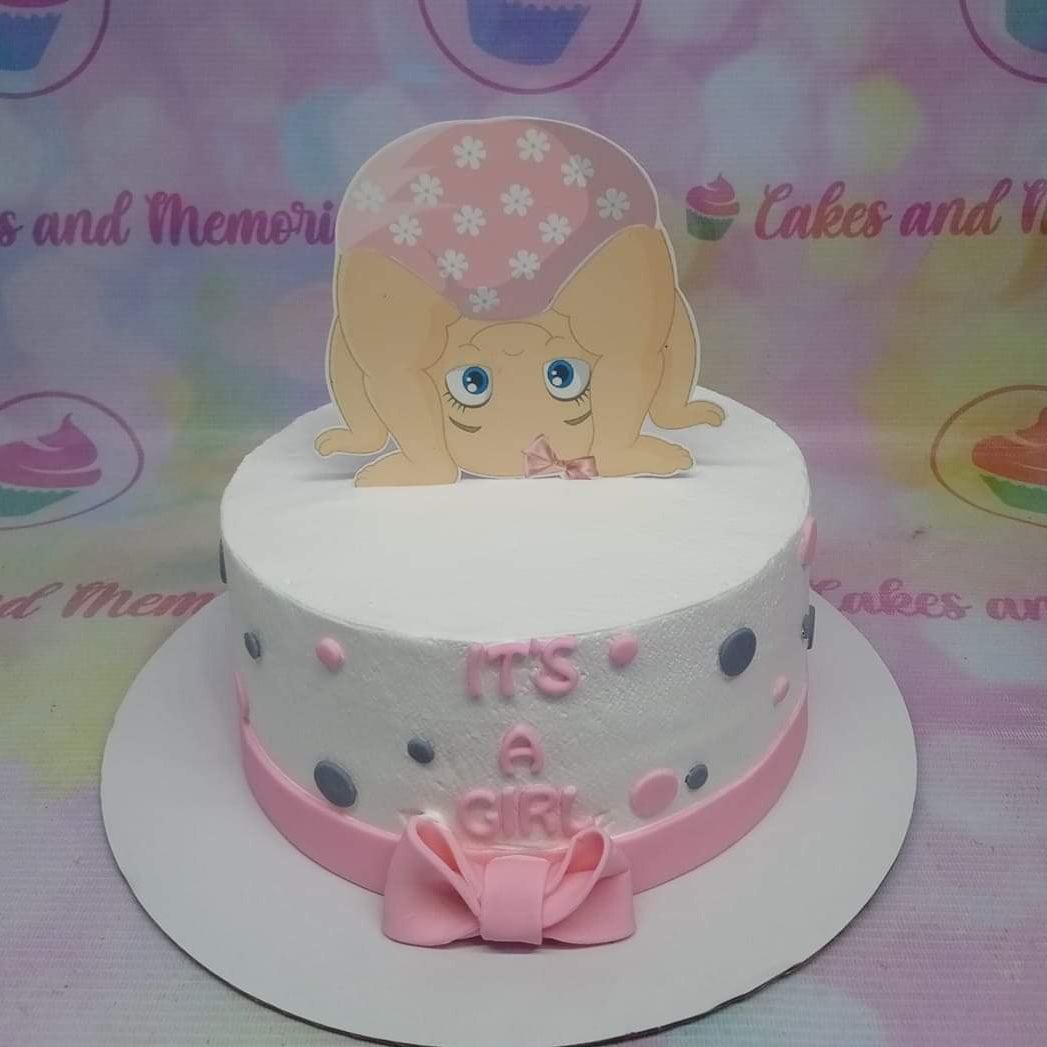 White round cake with pink and gray polka dots, a pink bow, and a large printout of a baby girl in a pink diaper.