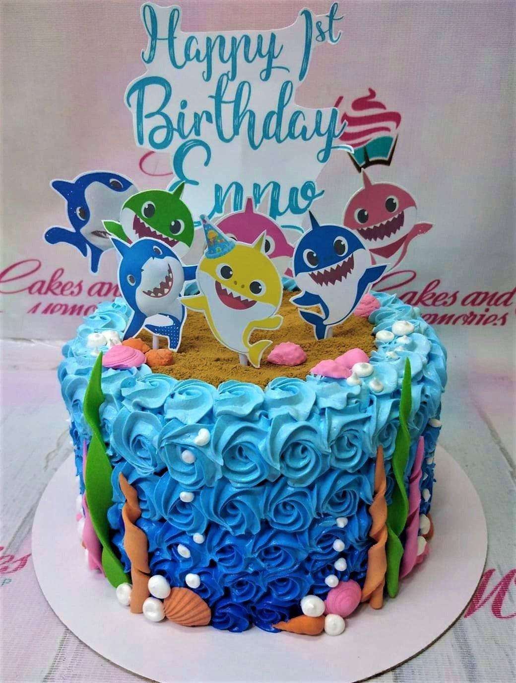 Baby Shark themed birthday cake with blue icing rosettes, sand-textured top, and colorful shark character printouts.