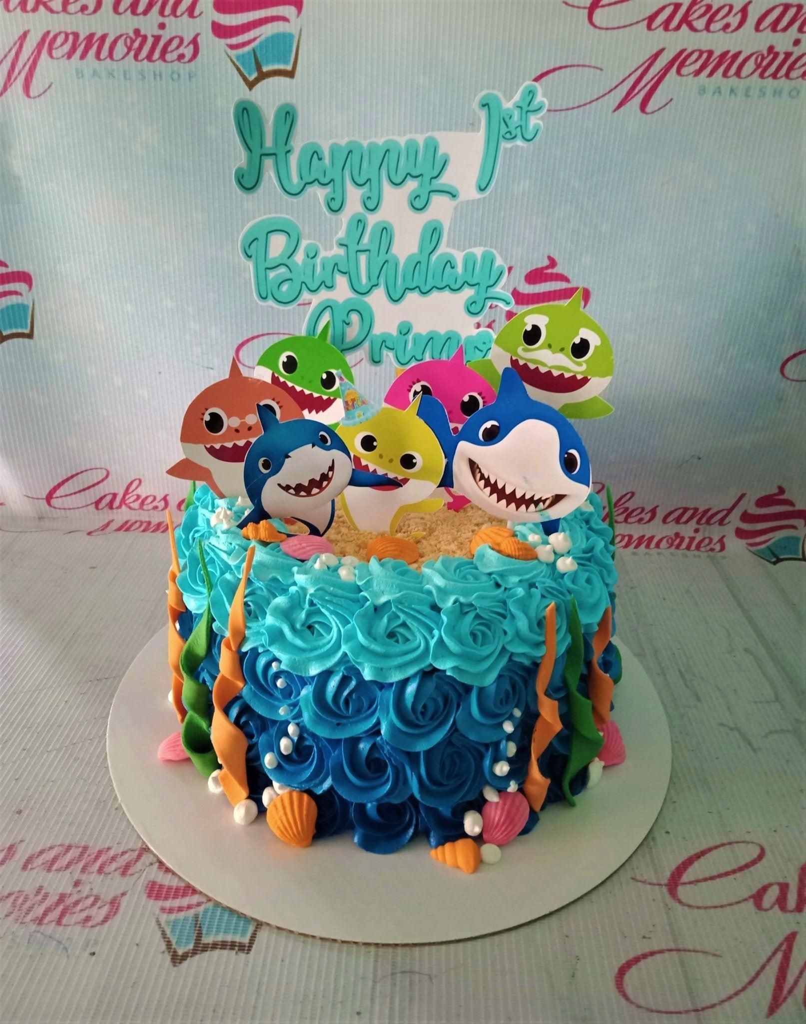 Blue ombre Baby Shark themed birthday cake with colorful shark printouts and edible sea decorations.