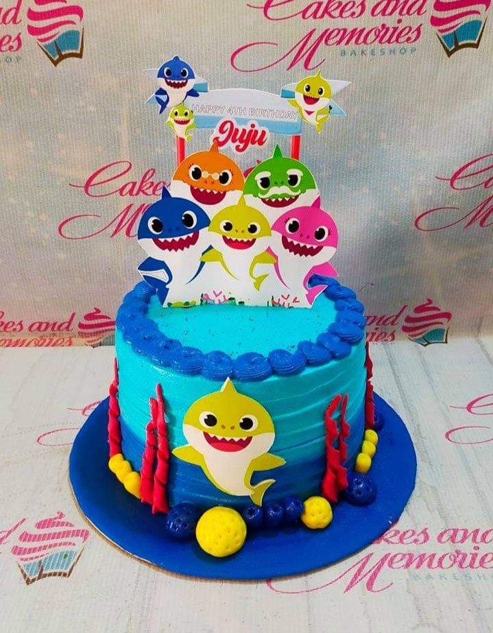 Blue Baby Shark themed birthday cake with colorful shark printouts and red gumpaste coral decorations.